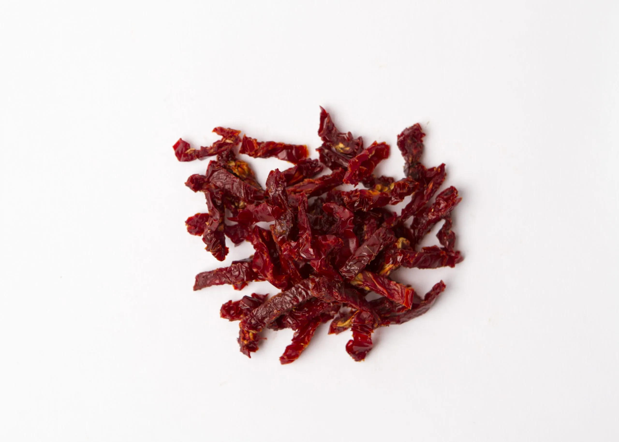 Traina® California Sun Dried Tomatoes, julienne Cut - small pile of sun dried tomatoes on white background.