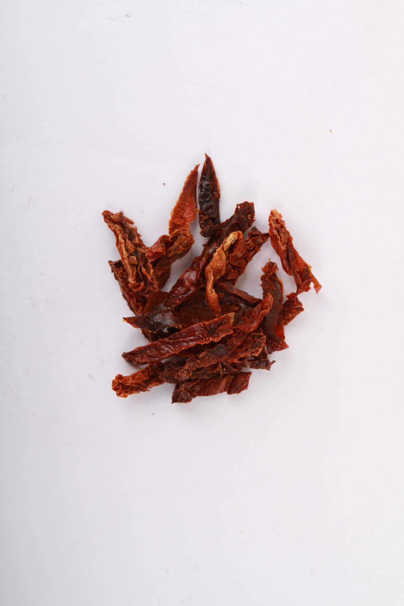 Natural California Sun Dried Tomatoes, no salt, julienne cut - small pile of sun dried tomatoes on white background.