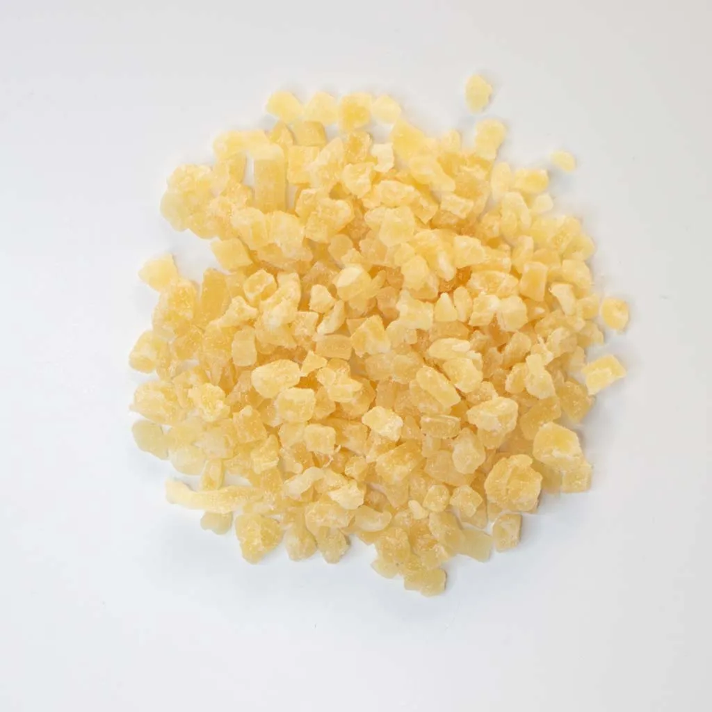 Traina® Dried Pineapple, Sweetened, with Sulfur, diced 8-10 mm - small pile of dried fruit on white background.