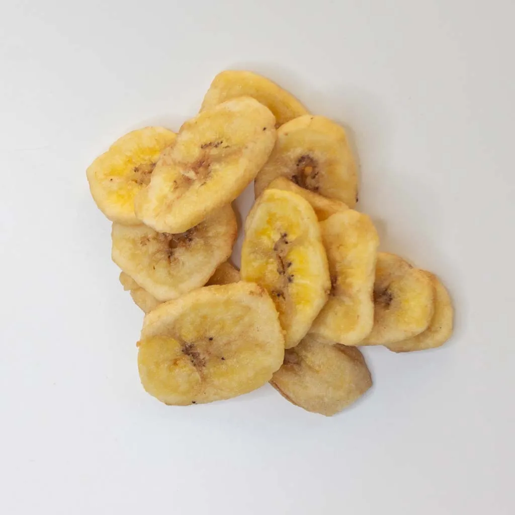 Traina® Dried Banana, Chips, sweetened - small pile of dried fruit on white background.
