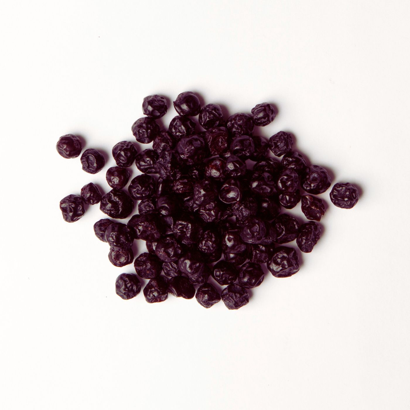 Traina® Dried Blueberries, Sweetened, whole - small pile of dried fruit on white background.