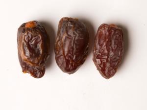 Traina® California Medjool Dates contains pits - small pile of dried fruit on white background.