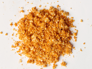 Traina® Organic Dried Orange, granules - small pile of dehydrated fruit on white background
